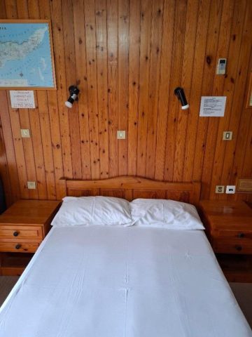 Room 1 Διπλό κρεβάτι στο Δωμάτιο 1 του EVDOXIA Hotel, με ξύλινο κεφαλάρι, κομοδίνα, φωτιστικά τοίχου και ξύλινες επενδύσεις.